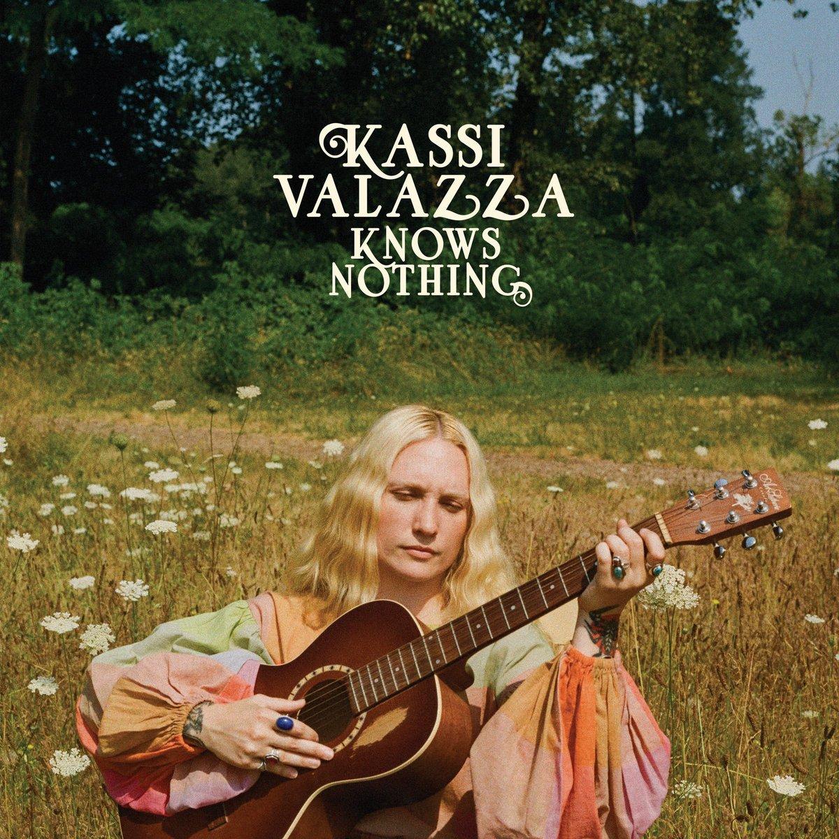 Album cover for Kassi Valazza Knows Nothing, depicting Kassi Valazza sitting in a field of wildflowers playing an acoustic guitar