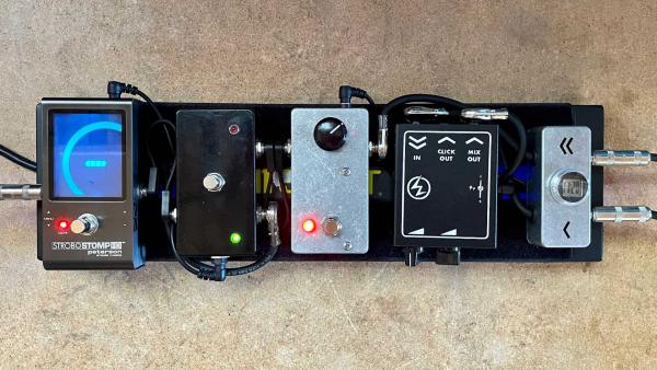 Pedalboard on workbench with a tuner, A/B box, boost pedal and bass preamp
