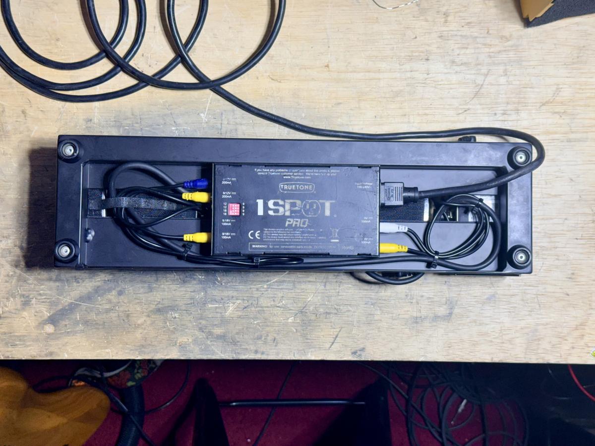 Underside of a guitar pedalboard showing a 1 Spot Pro power supply.